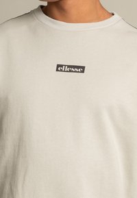 Felpa leggera grigia con collo rotondo, realizzata in tessuto morbido, con un logo rettangolare nero al centro e banda a coste nel collo.