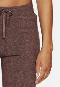 Pantalons de jogging en tricot marron avec une taille élastique et un cordon de serrage. La texture est douce et légèrement chinée, avec des détails de couture visibles.