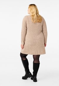 Vestido de punto acanalado beige con mangas largas, hasta la rodilla, combinado con botas negras hasta la rodilla. Textura suave, diseño simple, sin patrones adicionales.