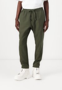 Olive green jogger pants with an elastic waistband and drawstring, featuring a relaxed fit and side pockets. Paired with white chunky sneakers.