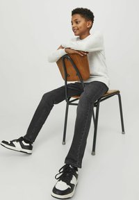 Vaqueros de mezclilla negros, camisa de manga larga gris claro y zapatillas en blanco y negro, sentado en una silla de madera con un marco de metal.