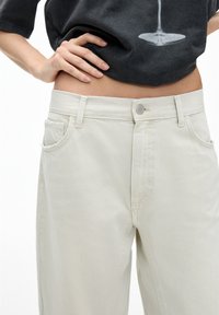 Beige högmidjade jeans i denim, med framfickor, en metallknappsstängning och en slät textur. Enkelt design utan synliga mönster.