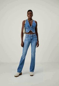 Light blue denim crop top with V-neck design, paired with light blue flared jeans. Model wears cream platform shoes and a small bag.