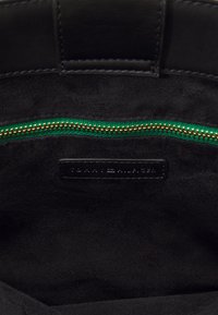 Intérieur d'un sac en daim noir avec une fermeture éclair en tissu vert et une étiquette en cuir noir cousue avec un nom de marque embossé.