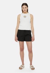 Top bianco senza maniche con logo blu, abbinato a pantaloncini neri con cordino. Il modello indossa sandali crema con suola testurizzata.