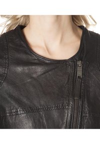 Gros plan d'une personne portant une veste en cuir noire avec une fermeture éclair verticale près de la clavicule.