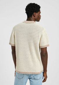 Kortärmad stickad tröja i krämfärg med ett mönster av textur, kontrasterande beige ribbad krage och ärmslut, med en avslappnad passform.