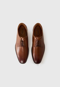 Zapatos de vestir de cuero marrón con un acabado suave, que presentan una punta redondeada, cierre con cordones y detalles de costura sutiles.