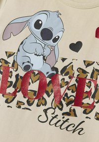 Jasno beżowa koszulka z nadrukiem postaci z kreskówki o dużych uszach, z czerwonym błyszczącym napisem "LOVE" na tle w panterkę.