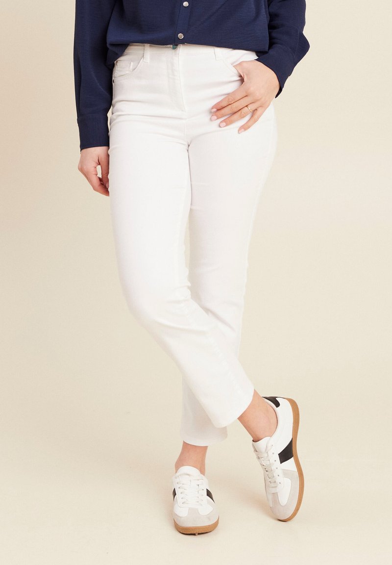 Weiße Baumwollmischungshosen mit schlanker Passform, fünf Taschen und sichtbaren Nähten. Kombiniert mit weißen Sneakers mit niedrigem Schnitt und schwarzen Akzenten.