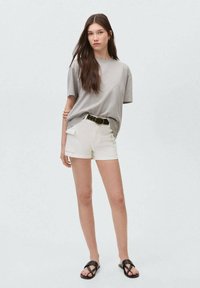 Ljusgrå, oversized t-shirt i kombination med vita shorts med sidfickor. Bärs med svarta sandaler och ett svart bälte. Slät textur.
