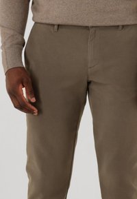 Brown, straight-leg trousers made of smooth fabric featuring front and back pockets, subtle stitching details, and a mid-rise waist.