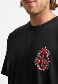 Czarny t-shirt z bawełny z wyraźnym czerwono-srebrnym wzorem węża z kolcami na przodzie. Okrągły dekolt i krótkie rękawy.