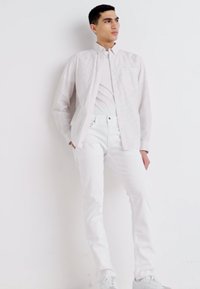White cotton button-up shirt with vertical stripes, paired with white jeans and white sneakers, modeled against a neutral background.