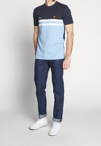 Tmavě modré a světle modré tričko s krátkým rukávem a vodorovnými bílými pruhy, s logem. Nošeno s tmavými džínami z denimu a b ílými teniskami.