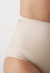 High-waisted beige underwear made from smooth fabric, featuring seamless edges and a simple design without ornamentation.