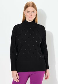 Svart stickad polotröja med en diamantmönster och små silverdetaljer. Ribbad nederkant och ärmar, med en avslappnad passform.