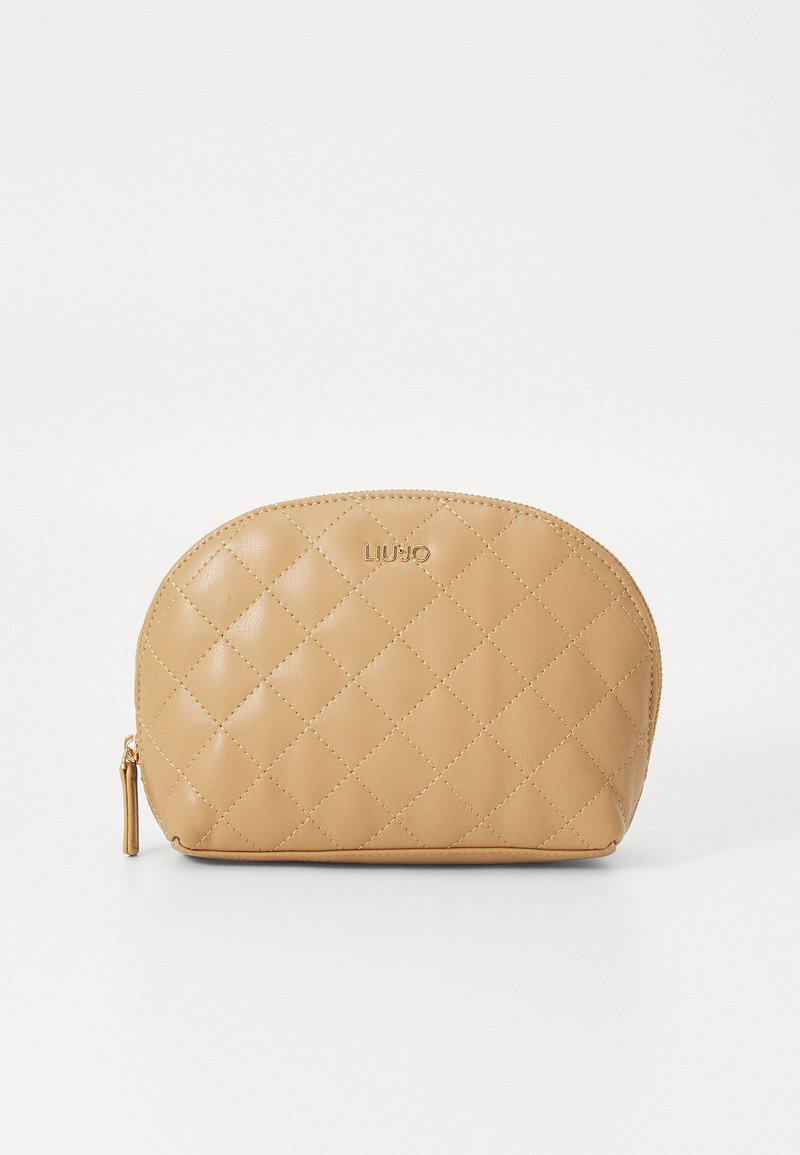 Bolsa cosmética acolchada en color beige, con forma redondeada, logotipo dorado en la parte superior y cierre con cremallera. Textura suave y brillante.