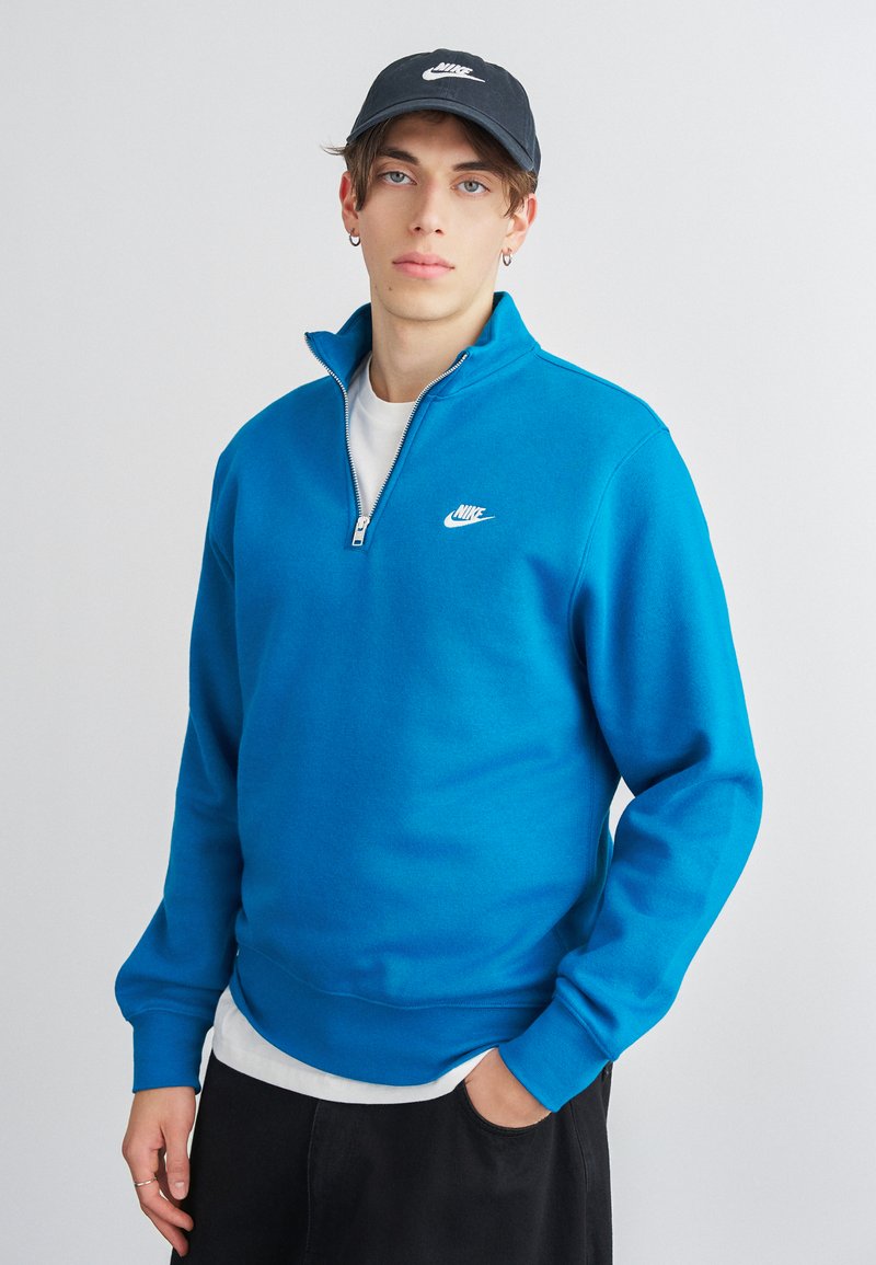 Μπλε φούτερ με φερμουάρ στα ¼, ριμπ μανσέτες και ελαστική μέση. Διαθέτει λευκό λογότυπο Nike στο αριστερό στήθος. Μαύρο καπέλο με λευκό λογότυπο.