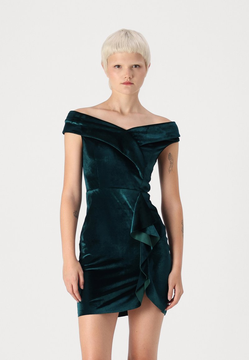 Robe en velours à épaules dénudées de couleur vert foncé, présentant un design enveloppé avec un volant cascade à l'ourlet et une texture lisse.