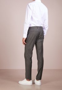 Pantaloni grigi su misura con una texture liscia, abbinati a una camicia bianca a maniche lunghe e sneaker bianche, visti da dietro.