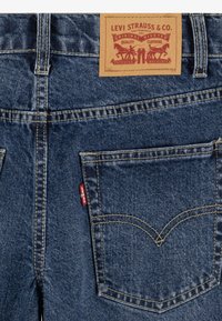 Zadnji žep modrih jeansov Levi's z značilno rdečo oznako Levi's in usnjenim vzorcem blagovne znamke nad pasom.