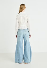 Blusa blanca con cuello rizado y cintura entallada, combinada con pantalones vaqueros de pierna ancha en azul claro. Incluye mangas largas y bolsillos traseros.