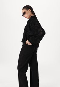 Svart teksturert oversized genser med gjennomsiktige paneler, kombinert med høyhåndte svarte straight-leg jeans. Modell med solbriller.