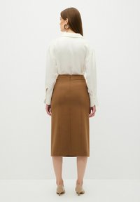 Witte blouse met lange mouwen en een bruine, kokerrok tot op de knie. De rok heeft een rits aan de achterkant en een gladde textuur.