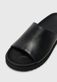 Sorte skinnslipper med bred rem og teksturert såle. Designet har en avrundet tå og en jevn finish.
