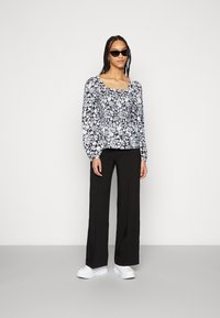Blusa com padrão floral em preto e branco, com mangas bufantes, decote quadrado e cintura franzida. Combinada com calças largas pretas e sapatilhas brancas.