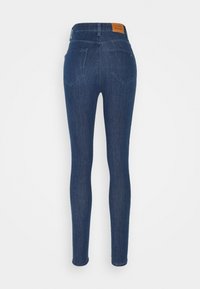 Jeans ajustados de mezclilla oscura con una pretina alta. Cuentan con dos bolsillos traseros y una etiqueta de cuero marrón con el logotipo en la parte trasera de la cintura.