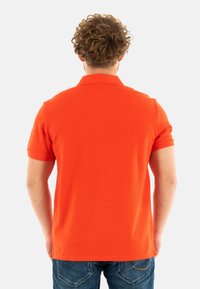 Polo de manga corta en algodón naranja brillante, con un cuello clásico y un dobladillo recto, combinado con unos vaqueros de denim azules.
