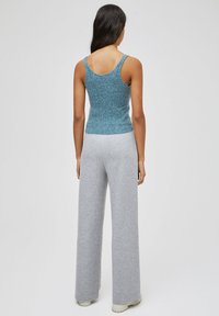 Teal top tank rajut dengan tali sempit dan pinggang pas, dipadukan dengan celana sweatpants lebar warna abu-abu muda. Kain rajut berbentuk tekstur.