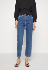 Light blue high-waisted jeans with a straight leg, frayed hem, and classic five-pocket design, paired with a black long-sleeve top.