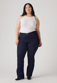 Mørkeblå denim vide jeans med en svak glans, med fem lommer og gul søm. Kombinert med en hvit tanktopp.