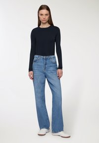 Granatowa bluzka z długim rękawem w połączeniu z jasnoniebieskimi, szerokimi spodniami z wysokim stanem; białe trampki dopełniają całość. Gładki materiał i wyblakłe detale.