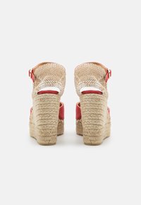 Klínové sandály s pleteným béžovým textilem, červenými textilními akcenty a přírodní jutu na podpatku. Obsahují řemínek kolem kotníku s kovovou sponou.