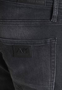 Vaqueros de denim gris oscuro con un acabado texturizado, con una etiqueta negra de goma que muestra "Antony Morato" y el logo "AM" en el bolsillo trasero.