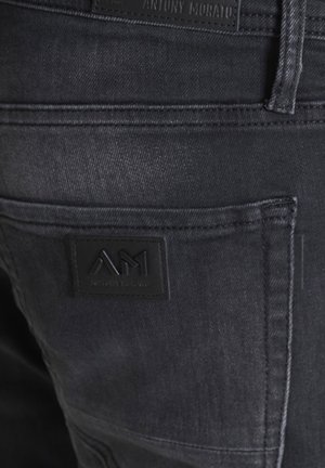 Jeans in denim grigio scuro con finitura testurizzata, dotati di un'etichetta nera in gomma con la scritta "Antony Morato" e il logo "AM" sulla tasca posteriore.