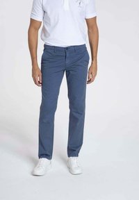 Pantalons en coton bleu pour homme avec une coupe slim, texture lisse, quatre poches et une fermeture à bouton, associés à des baskets blanches.