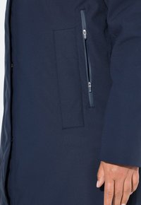 Námorně modrý kabát vyrobený z hladkého materiálu, s kapsou na zip, jednobarevným vzorem a jednoduchým, rovný střihem.