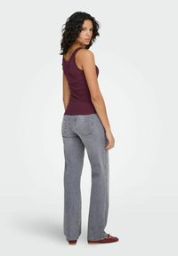 Bordeaux ribgebreide tanktop met kanten randen, gecombineerd met lichtgrijze uitlopende jeans en rode schoenen, gezien van achteren.