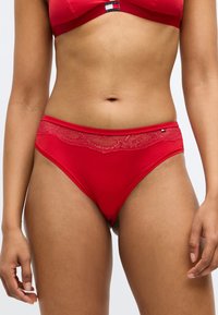 Røde hipsterundertøj med en blomsterlacemønster i taljen og glat stof. Designet inkluderer en lille logoaccent på siden.
