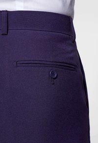 Pantalones en navy con corte entallado y frente plano, que presentan un bolsillo lateral con cierre de botón y una tela lisa y texturizada en un diseño ajustado.