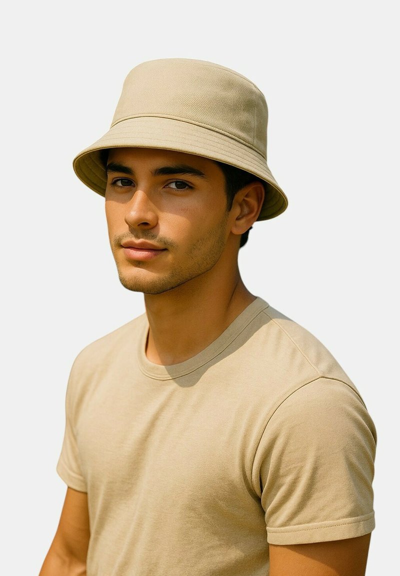 Beige Baumwoll-Bucket-Hut mit breiter, nach unten geneigter Krempe, kombiniert mit einem schlichten beige-farbenen T-Shirt in lockerer Passform.