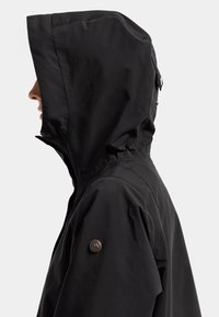 Svart vattentät jacka med huva, med en strömlinjeformad design, jämn textur och en logotypdetalj på vänster axel.