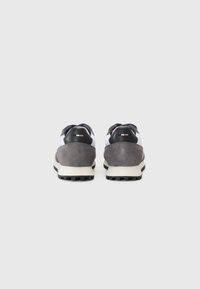 Sport shoes with a grey suede heel, black accents, white fabric detailing, and a textured rubber sole, viewed from the back.