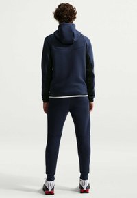 Μπλε ναυτικό φούτερ με κουκούλα και μαύρες πλαϊνές ρίγες, σετ με αντίστοιχο στενό παντελόνι φόρμας, απαλής υφής και κομψού σχεδιασμού.