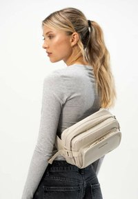 Borsa a tracolla beige con più scomparti, design elegante, finitura testurizzata sottile e tracolla regolabile, indossata in vita.